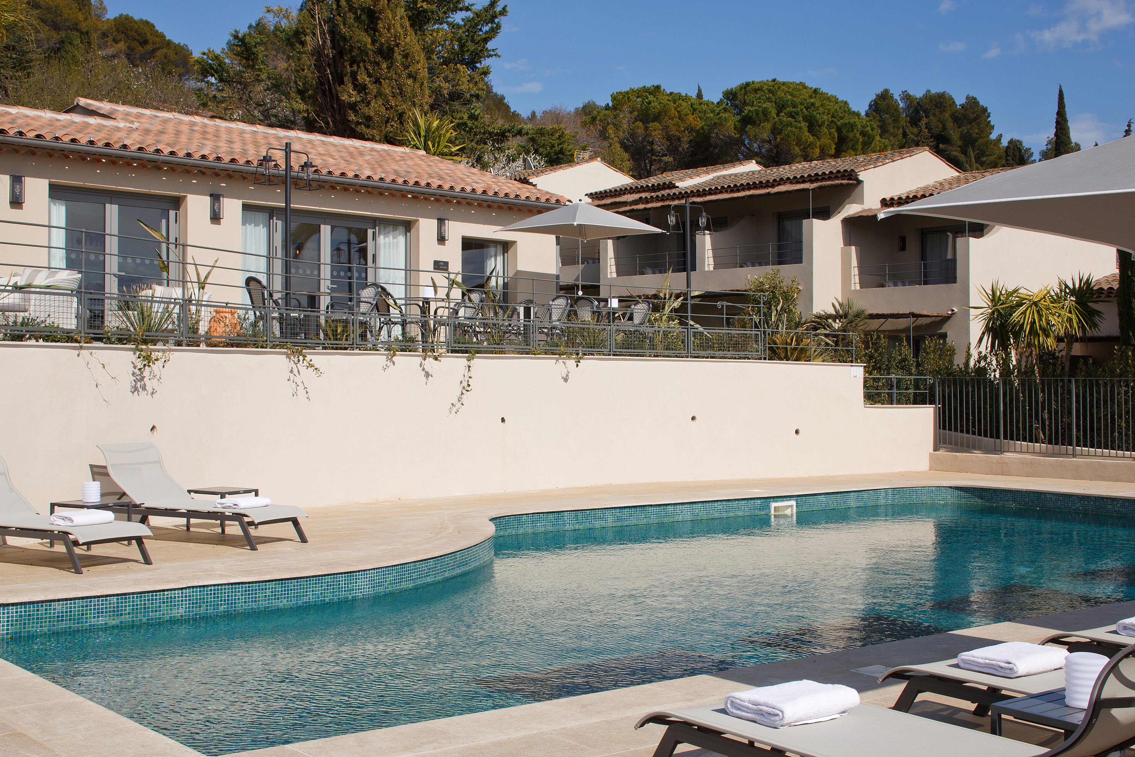 A pool area with lounge chairs and umbrellas, surrounded by buildings with tiled roofs.