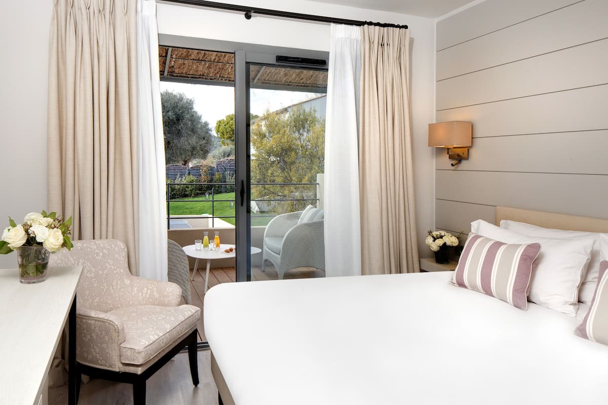 A hotel room with a bed, a chair, a small table, and a view of a garden through a sliding door.