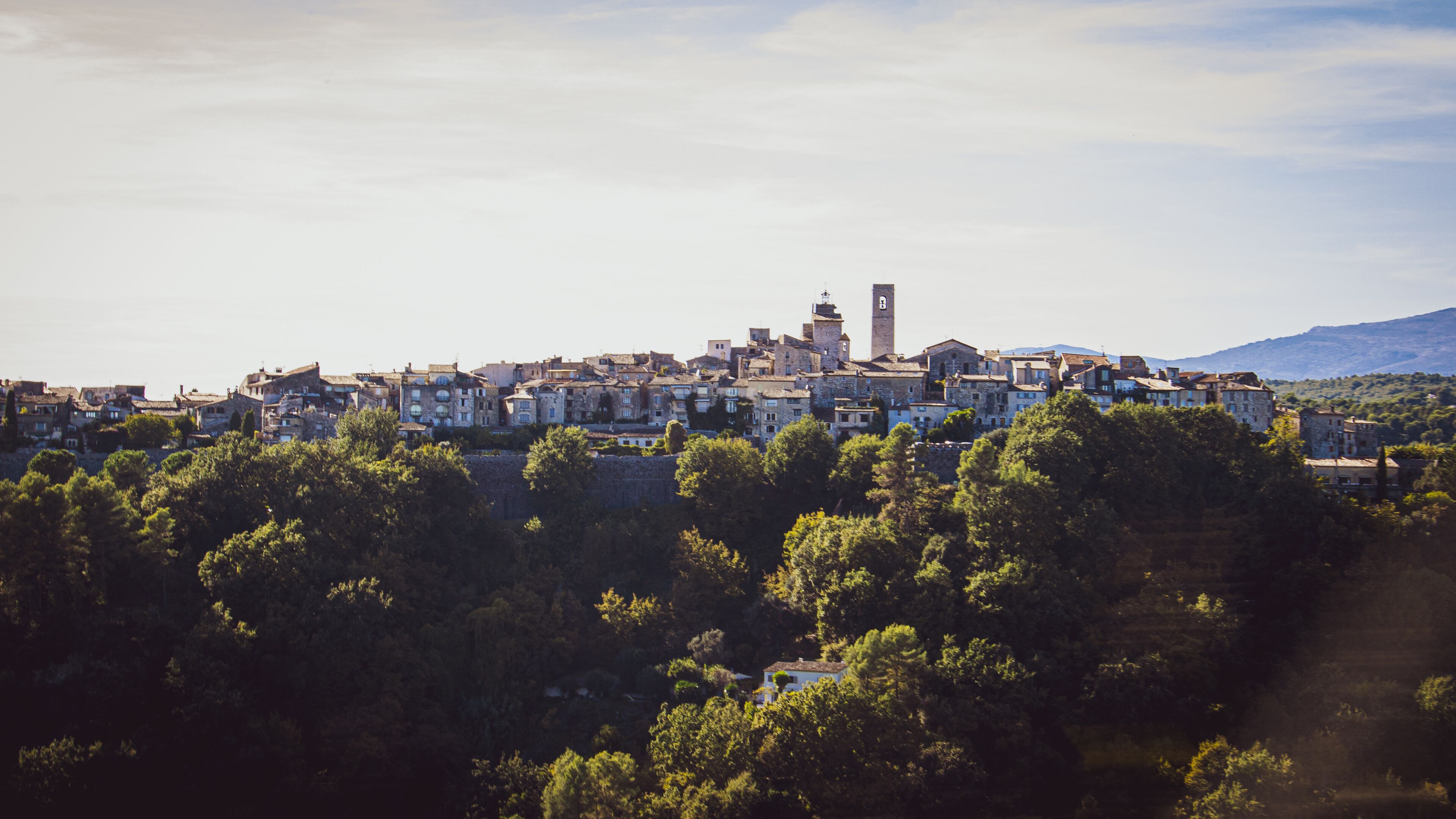 A historic town with stone buildings, a prominent tower, and lush greenery in the foreground.