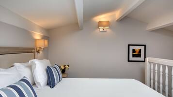 Un dormitorio ordenado con cama, almohadas, una mesita de noche con un florero y un cuadro en la pared.