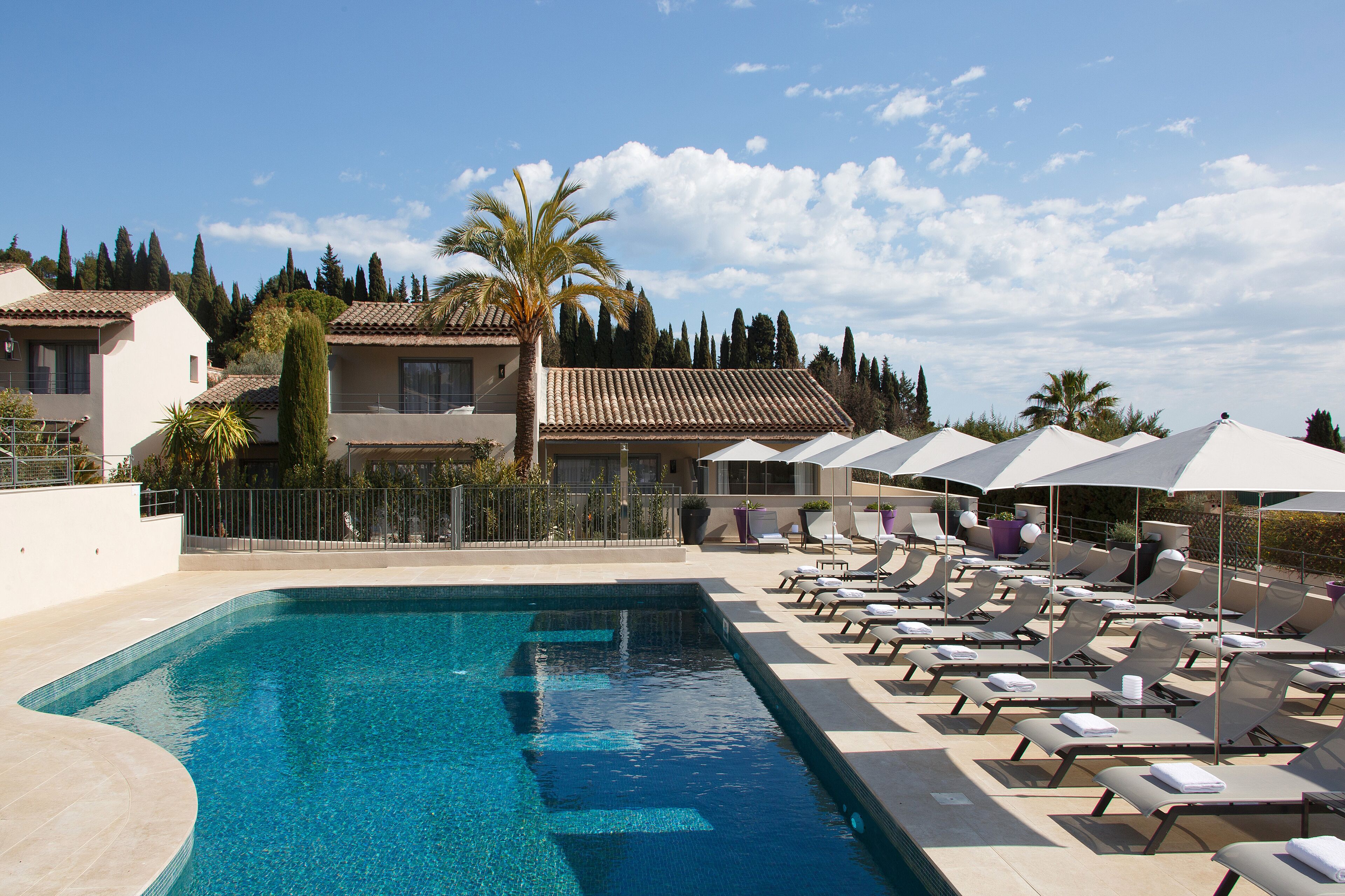 A swimming pool with lounge chairs and umbrellas, surrounded by buildings and trees.