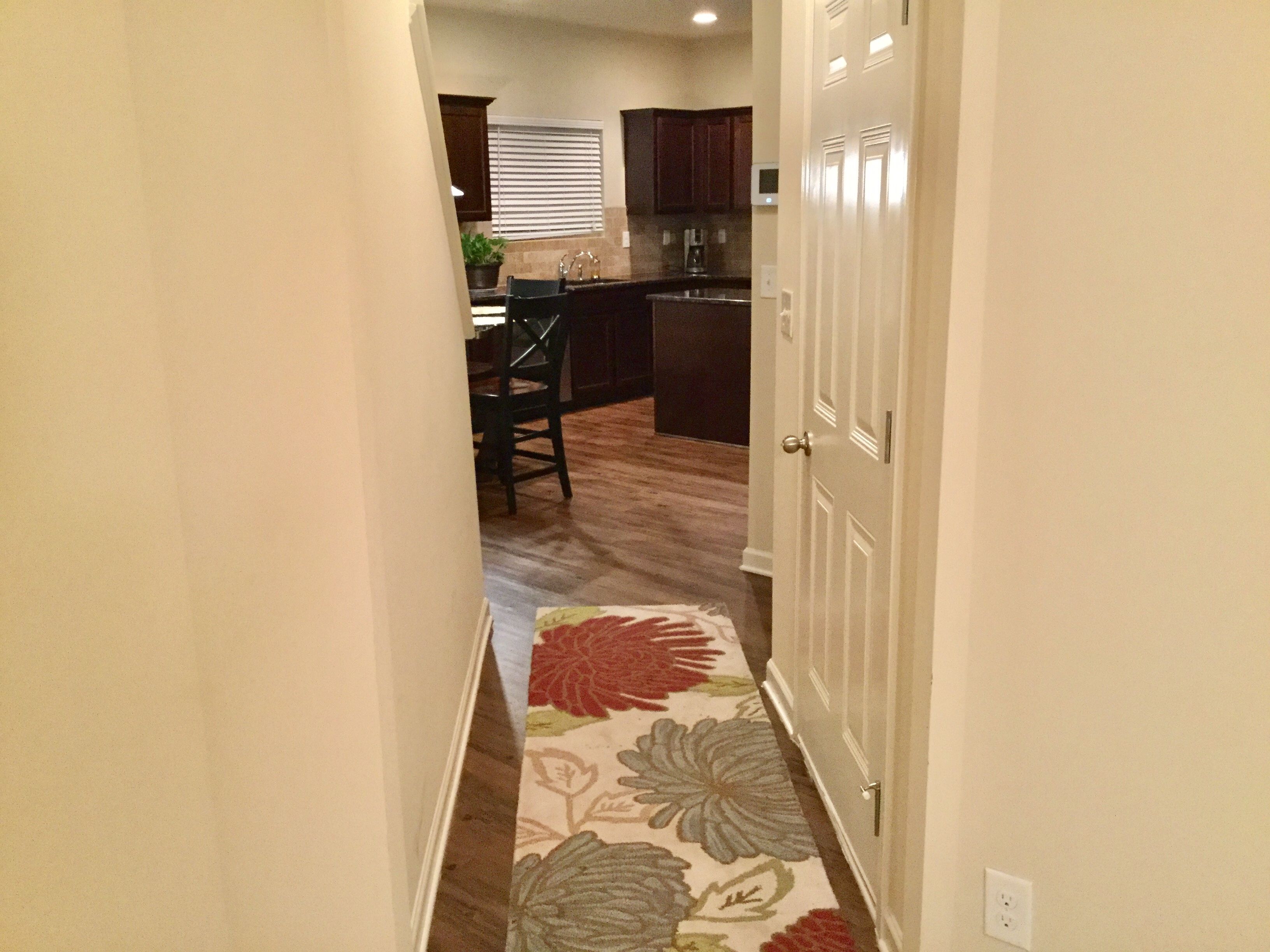 A narrow hallway leading to a kitchen area with wooden flooring and a floral-patterned rug.