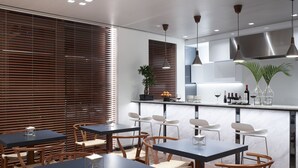 Un comedor moderno con sillas de madera y mesas negras, una barra con sillas blancas y una cocina con electrodomésticos de acero inoxidable.
