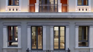 Un edificio de varios pisos con fachada simétrica, que presenta un balcón central con barandilla ornamental, ventanas regularmente distribuidas y un estilo arquitectónico uniforme.