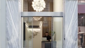 Una entrada de hotel moderna con una recepción, una lámpara de araña grande y una puerta de cristal.