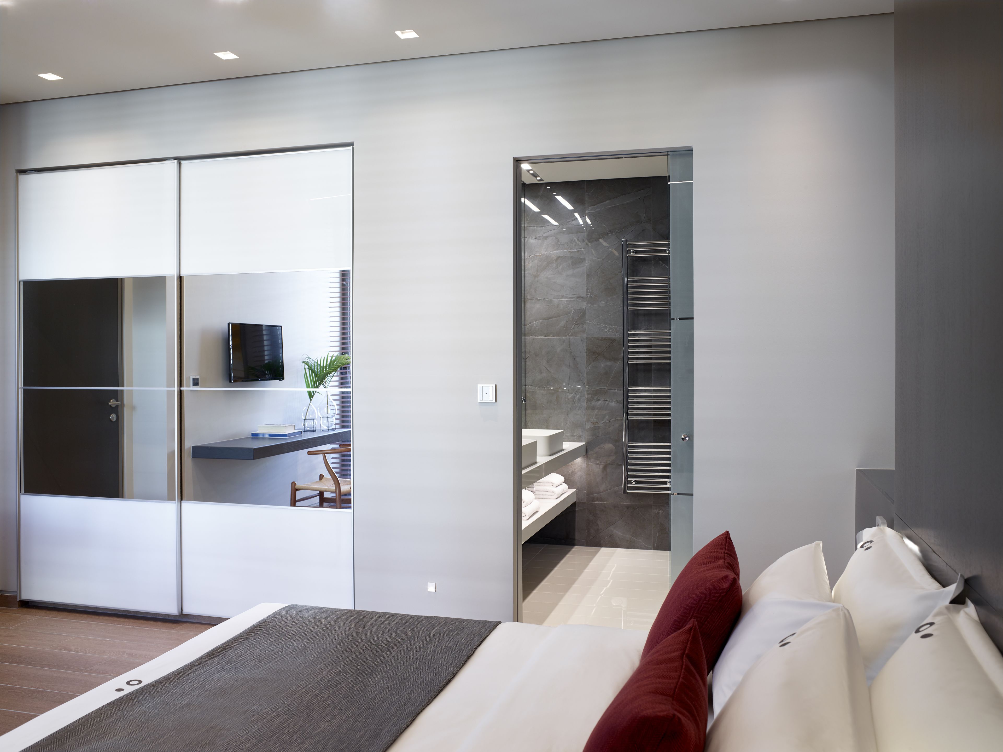 A modern bedroom with a bed, a desk, and a walk-in closet.