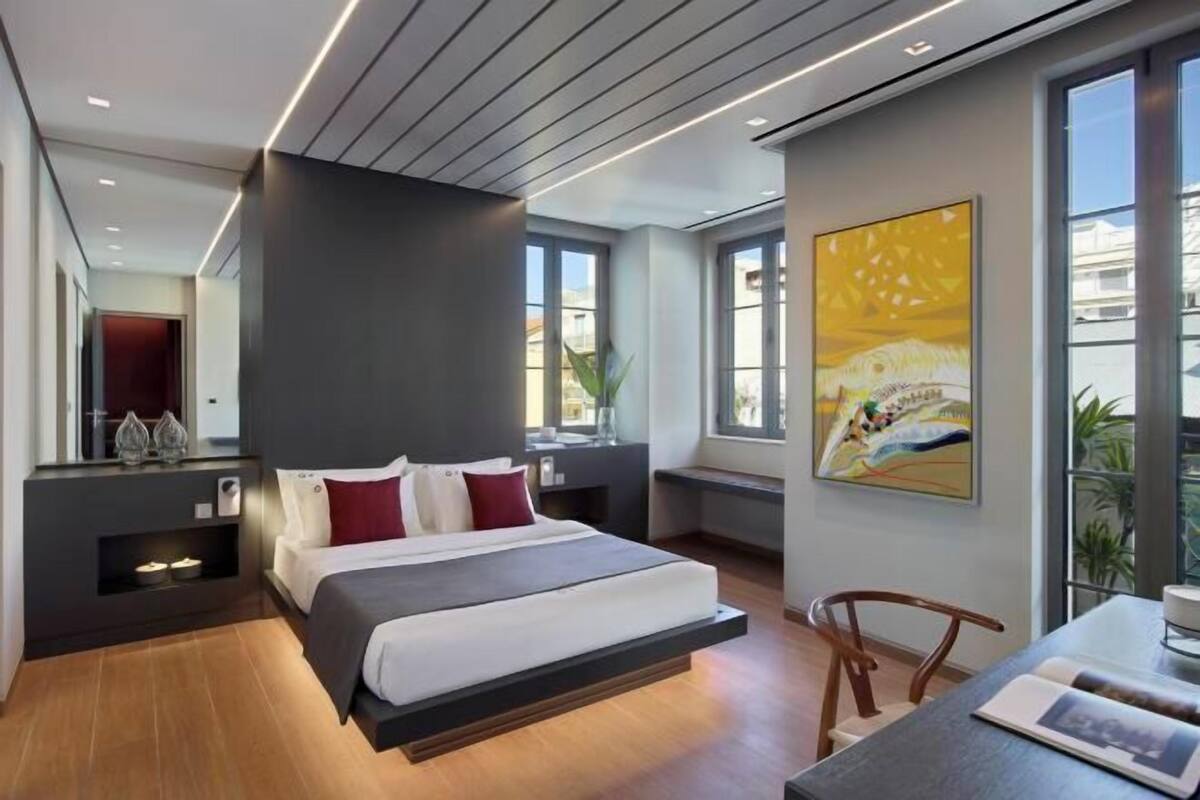 Ein modernes Hotelzimmer mit einem Bett, einem Schreibtisch, einem Sessel und einem großen Fenster.