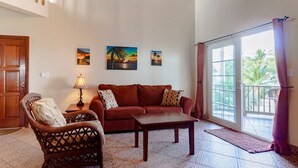 A living room with a wooden door, a sofa, a chair, a table, and a window with a view of palm trees. - Ocean Front Condo - just steps from the beach!  Gold Standard Approved (San Pedro)