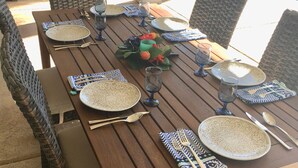 A wooden dining table set for six with plates, cutlery, and glasses.