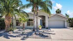 A single-story house with a garage, palm trees, and a well-maintained garden.