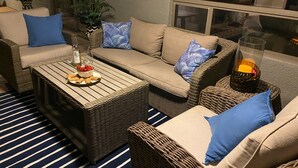 A cozy outdoor seating area with wicker furniture, a table with snacks, and a glass of drink.
