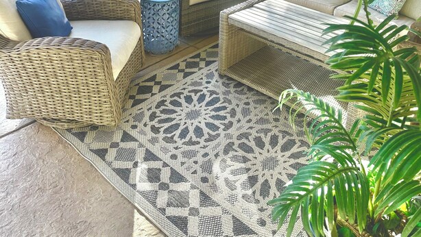 A covered outdoor seating area with wicker furniture, a pool, and a view of a backyard with a lawn and palm trees.