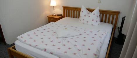 A neatly made bed with a floral bedspread, a wooden headboard, a bedside lamp, and a small bedside table.