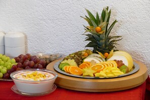 A fruit platter with a variety of fruits and a bowl of yogurt parfait on a red tablecloth.