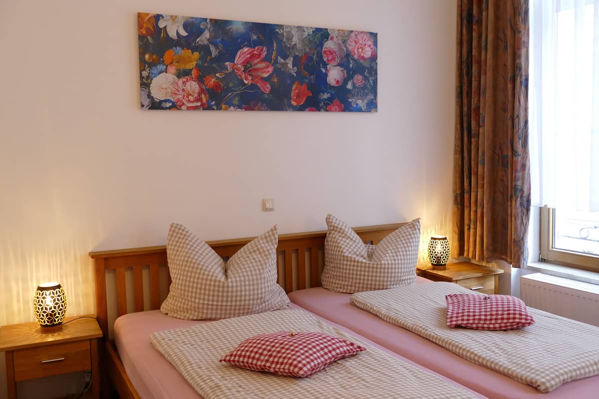 Una cama doble con ropa de cama a cuadros, un cuadro floral en la pared y una ventana con cortinas.
