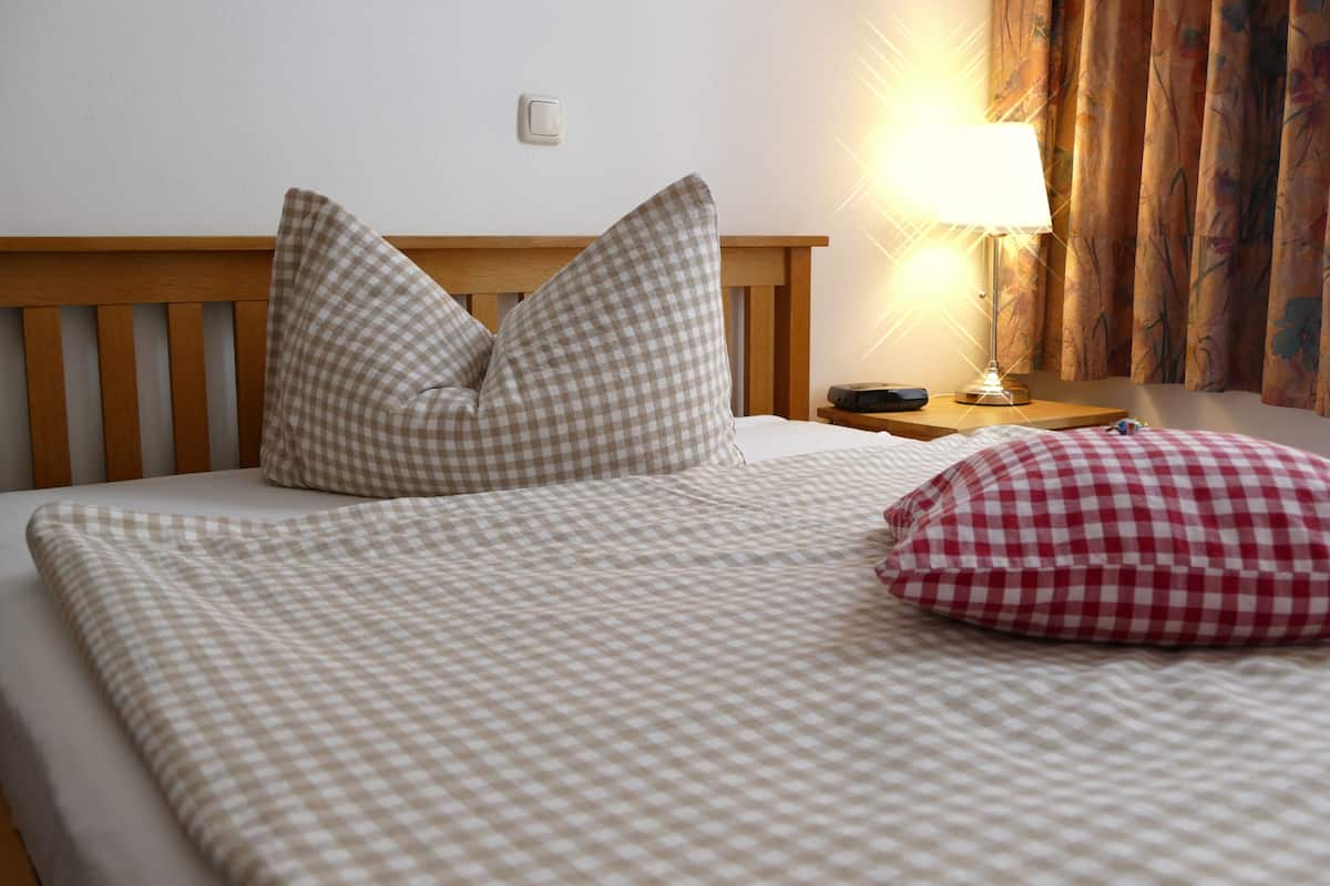 Una cama bien hecha con ropa de cama a cuadros, un cabecero de madera y una mesita de noche con una lámpara.