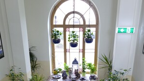 Una escalera con barandilla de madera lleva a un cuarto con piso de baldosas y una ventana con plantas colgantes.