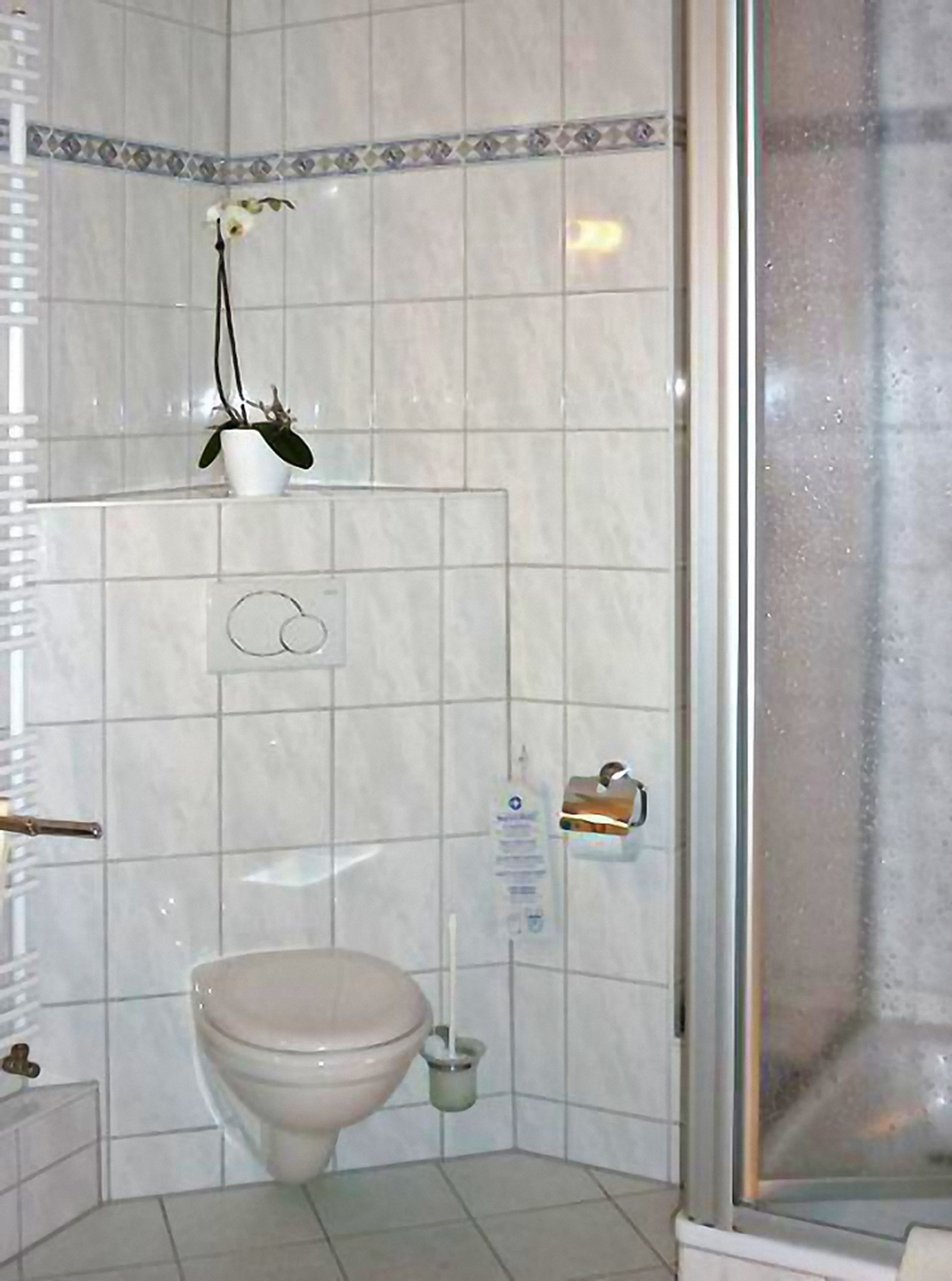 A bathroom with a toilet, a bidet, a hand dryer, and a small shelf with a potted plant.
