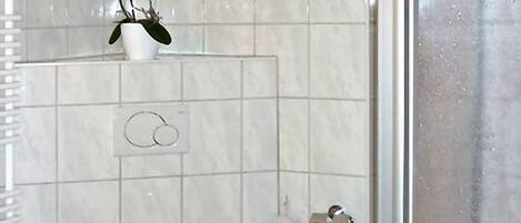 A bathroom with a toilet, a bidet, a hand dryer, and a small shelf with a potted plant.