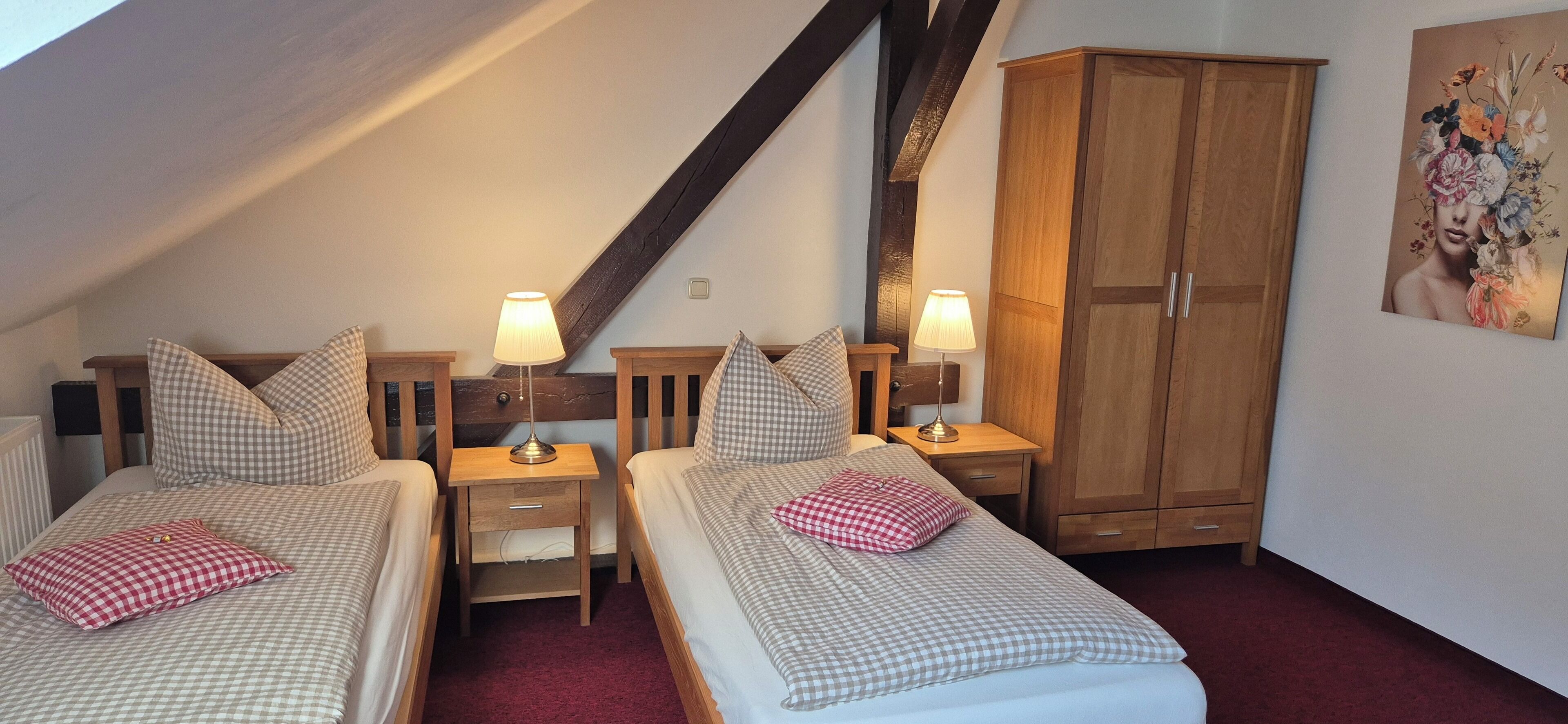 A bedroom with two beds, wooden nightstands, lamps, a wardrobe, and a painting on the wall.