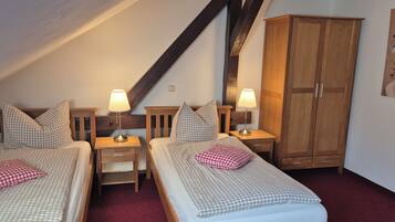 A bedroom with two beds, wooden nightstands, lamps, a wardrobe, and a painting on the wall.