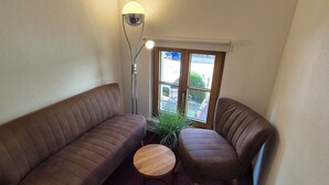 Una habitación de esquina con un sofá marrón, una mesita redonda pequeña y una lámpara de pie.