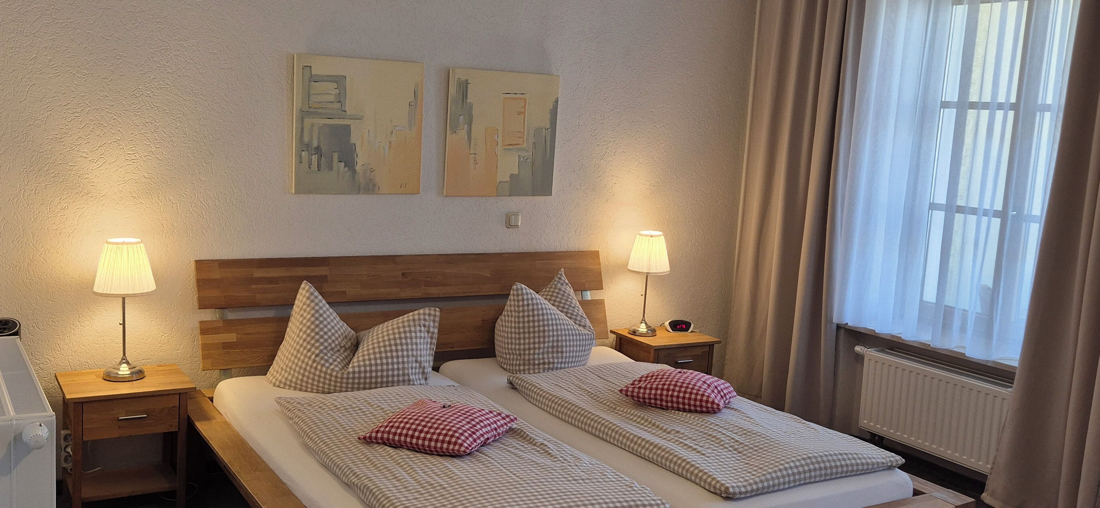 Une chambre d’hôtel avec deux lits, une literie à motifs à carreaux, deux lampes de chevet, une tête de lit en bois et deux tableaux abstraits accrochés au mur.