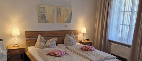 Une chambre d’hôtel avec deux lits, une literie à motifs à carreaux, deux lampes de chevet, une tête de lit en bois et deux tableaux abstraits accrochés au mur.