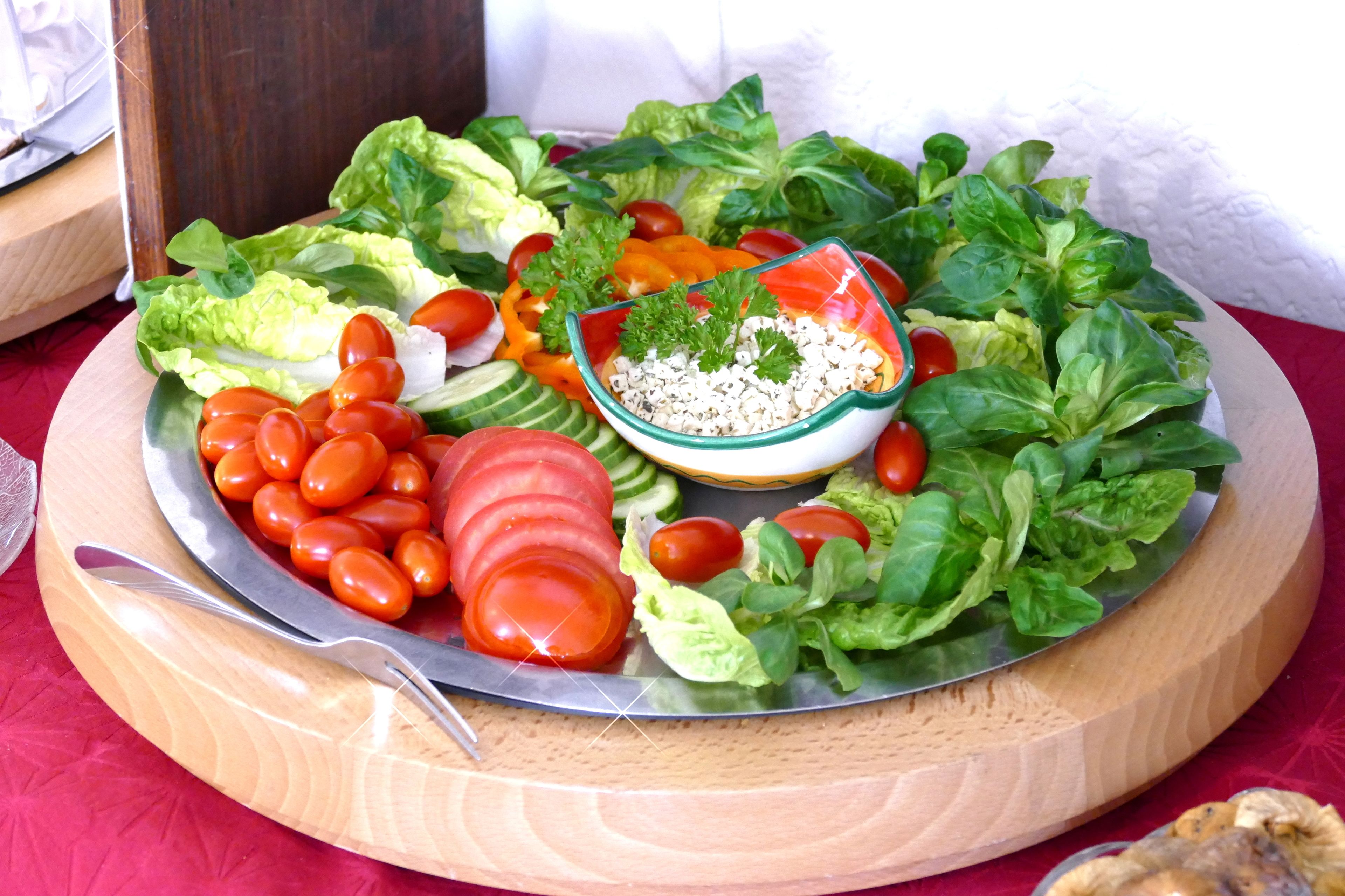 Uma travessa de madeira com diversos vegetais frescos e uma saladeira.