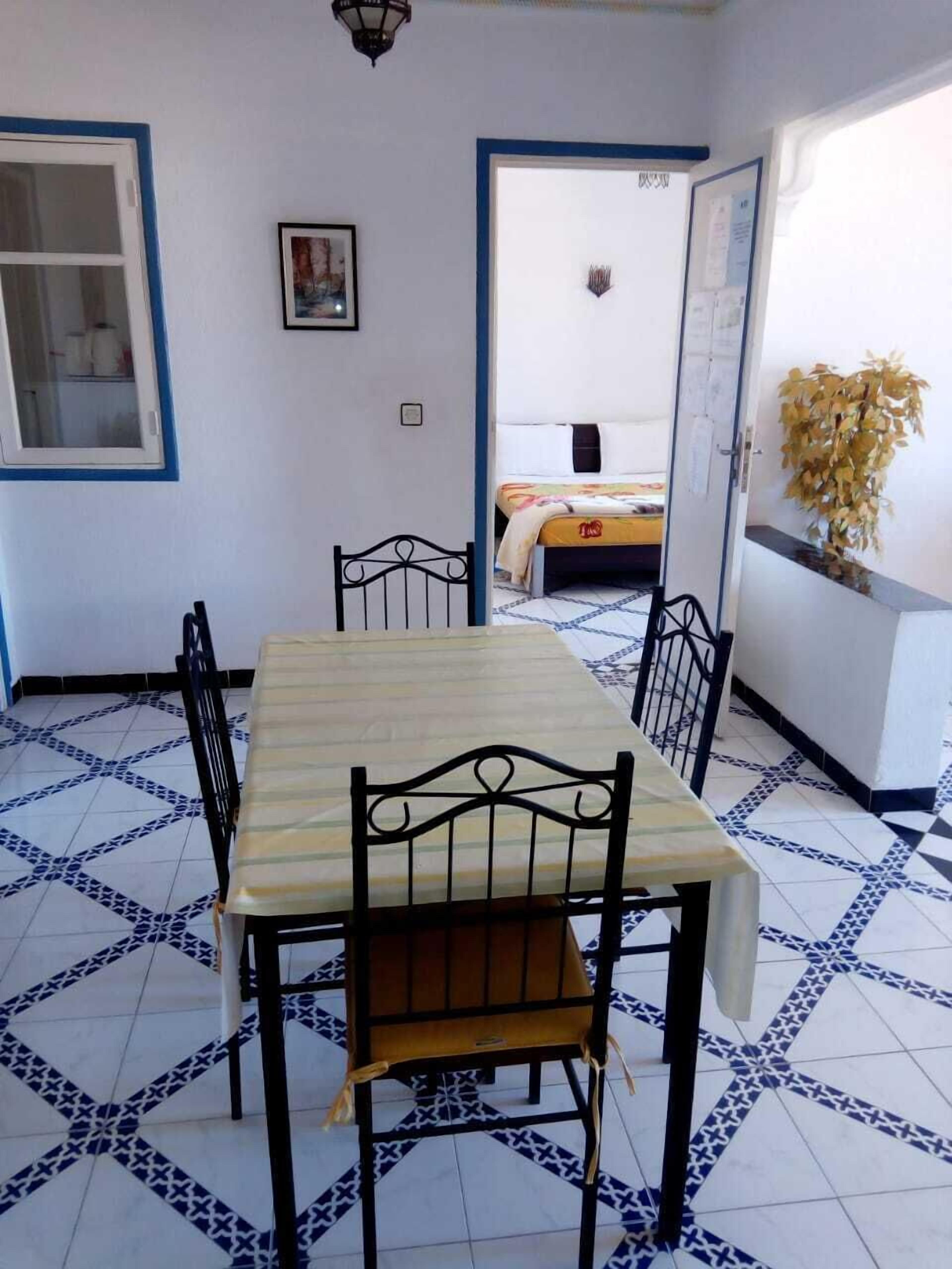 A dining area with a table and chairs, a bed in the background, and a tiled floor.