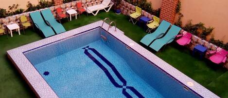 Piscina rectangular con borde de azulejos, rodeada por un muro de ladrillo y una pequeña zona de césped.