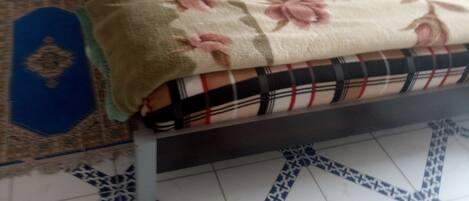 Una cama con manta estampada, cabecera y mesita de noche con lámpara.