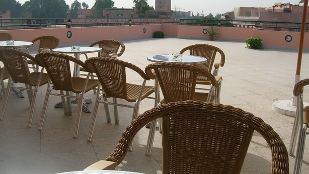 An outdoor seating area with wicker chairs and tables, a clock, and a view of a tower in the background. - Résidence Touristique Koutoubienne (Marrakech)