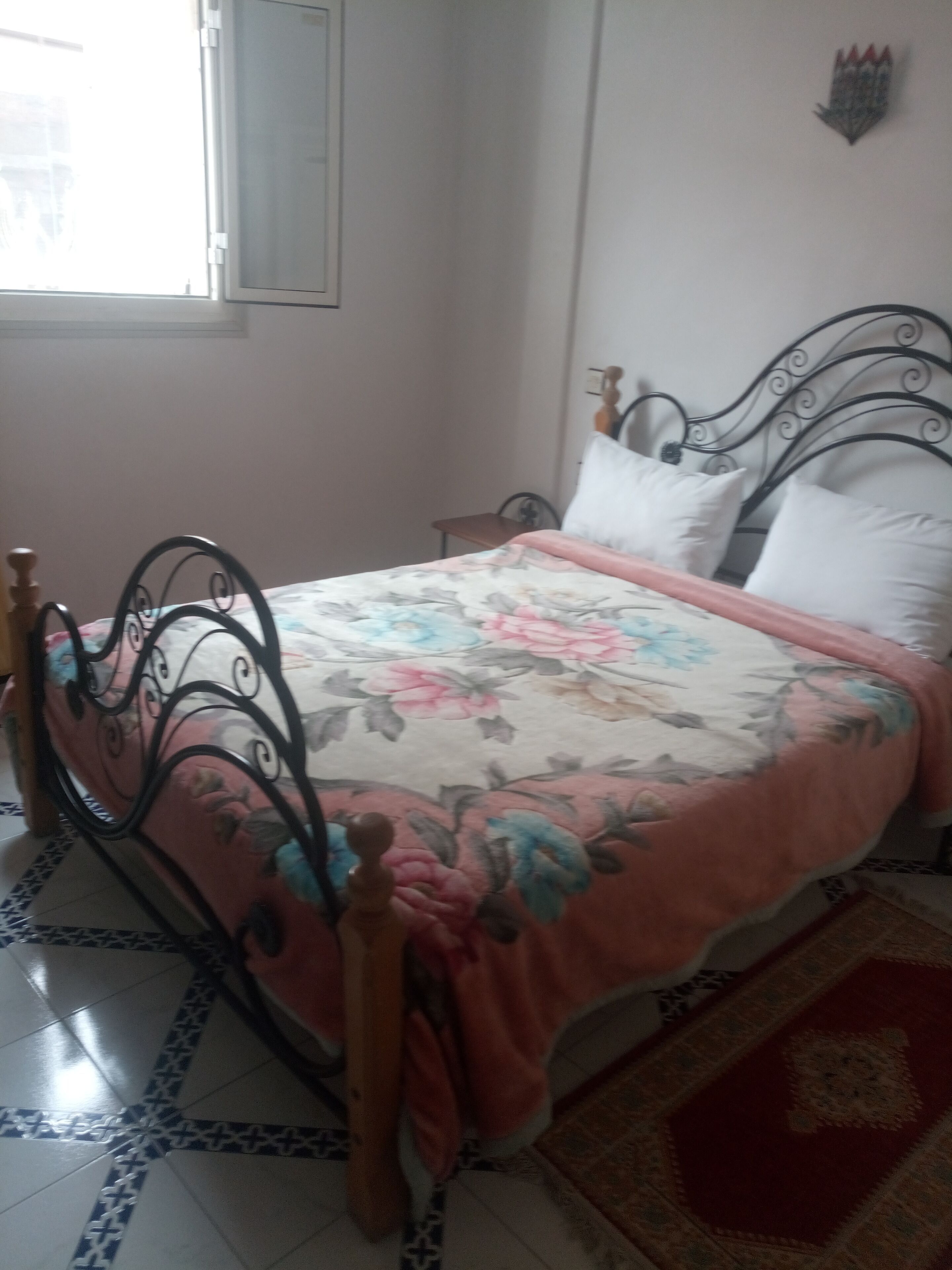 Una cama con colcha floral, cabecero de madera y alfombra roja.