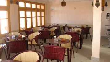 Un comedor con varias mesas y sillas redondas, ventanas amplias y apliques decorativos en la pared.