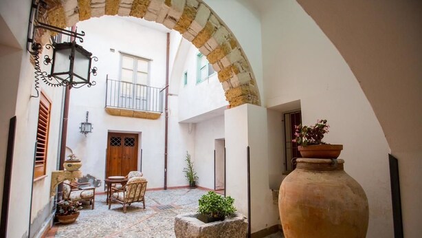 An interior courtyard with a stone bench, a large vase, and a rustic wooden door. - Palazzo Raho (Cefalù)