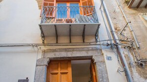 A building with a wooden door, a balcony with metal railings, and a stone archway. - Palazzo Raho (Cefalù)