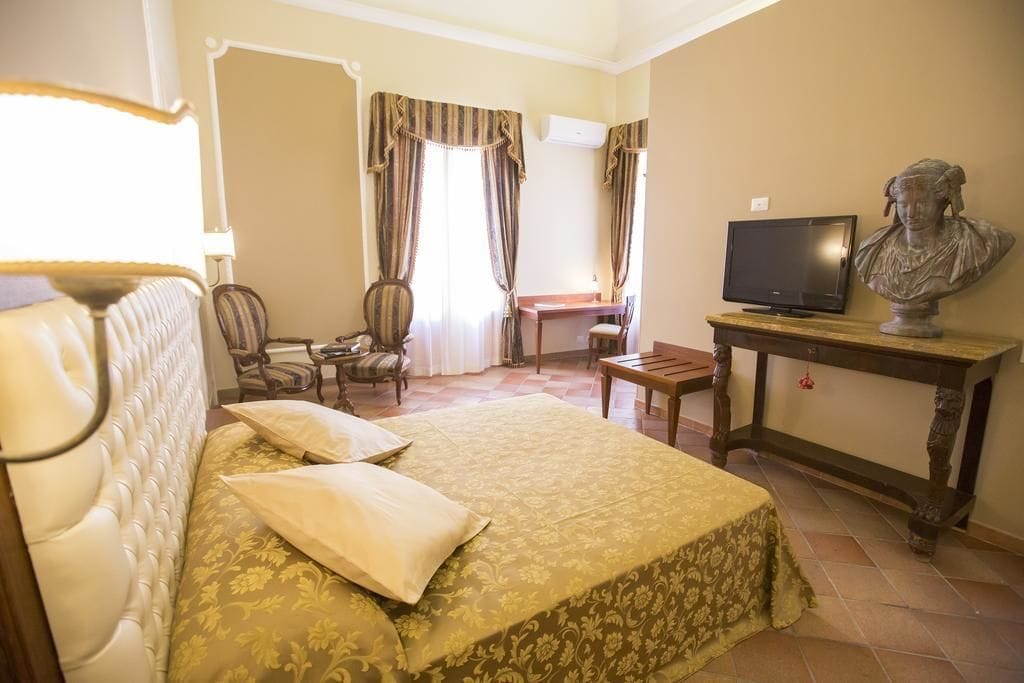 A hotel room with a bed, a desk, a television, and a bust on a table.