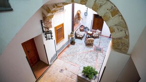 An interior courtyard with stone flooring, a wooden door, and a seating area with chairs and a table. - Palazzo Raho (Cefalù)