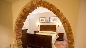 A bedroom with a brick archway, a wooden bed, a nightstand, a dresser, and three framed pictures on the wall. - Palazzo Raho (Cefalù)