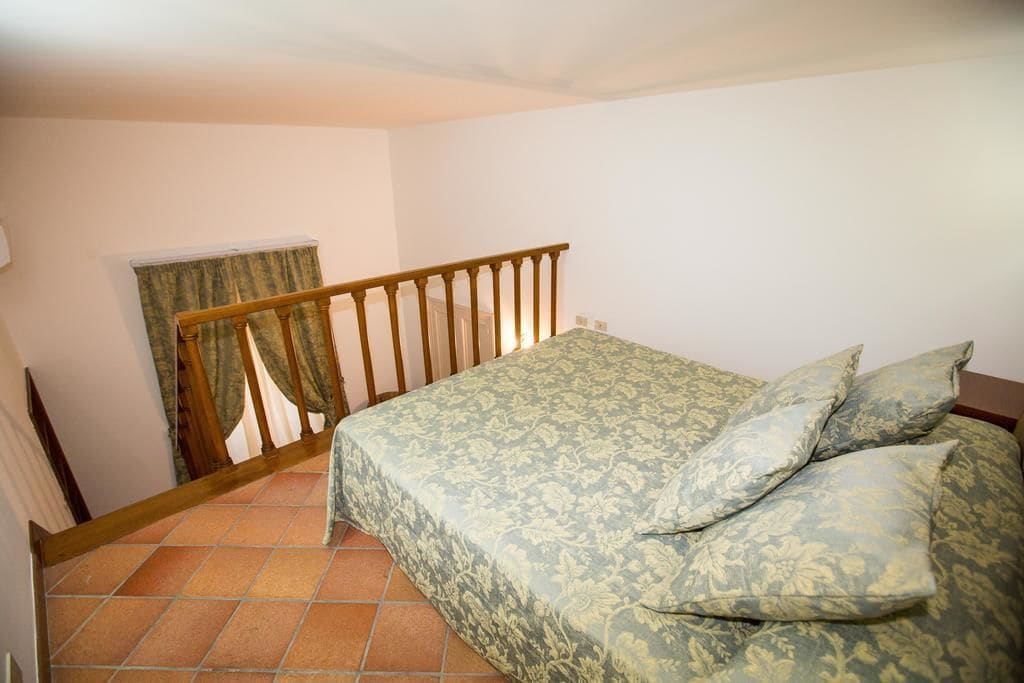 A bedroom with a bed, a wooden railing, and a window with curtains.