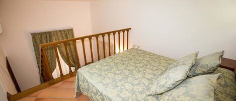 A bedroom with a bed, a wooden railing, and a window with curtains.