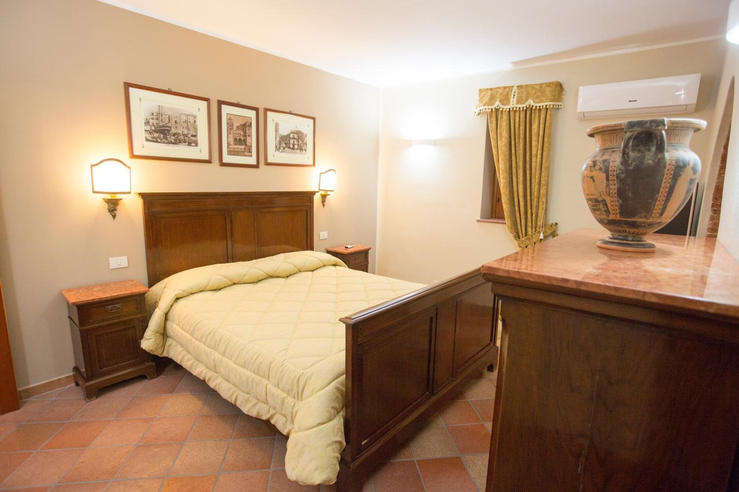 Een slaapkamer met een houten bed, nachtkastjes, een grote vaas en ingelijste foto's aan de muur.