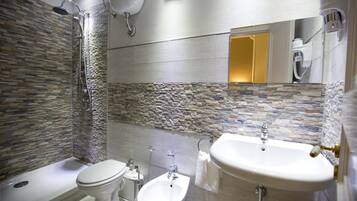 Ein modernes Badezimmer mit einer Wand aus Steinmosaik, einer Badewanne, einer Toilette, einem Bidet und einem großen Waschbecken.