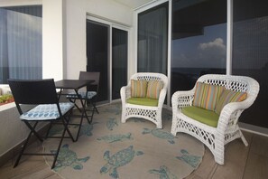 Een balkon met twee witte rieten stoelen, een klein tafeltje en een stoel met blauw-witte patronen.