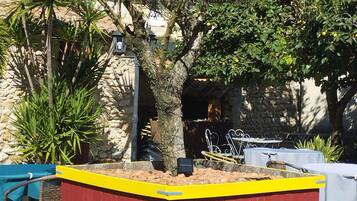 A red and yellow outdoor seating area with a stone wall backdrop, surrounded by various plants and trees.