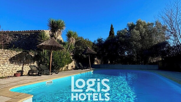 Une piscine d’un bleu éclatant, bordée d’un mur de pierre et entourée de chaises longues, le tout niché au milieu des arbres et adossé à un bâtiment en pierre.