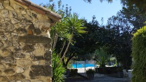 Un bâtiment en pierre avec un toit en tuiles, un chemin en pierre et une vue sur une piscine.