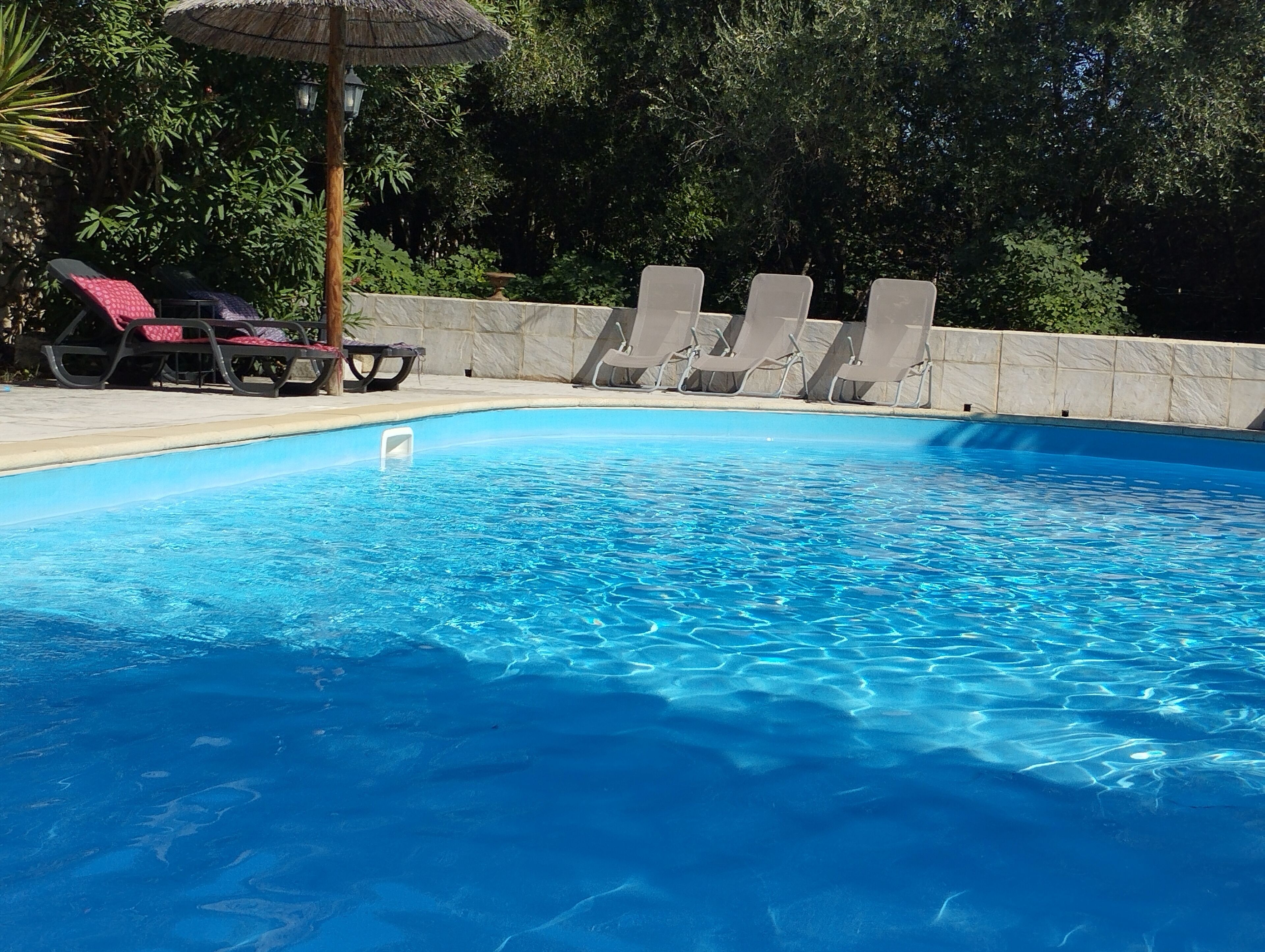 A swimming pool with clear blue water, surrounded by lounge chairs and a stone wall.