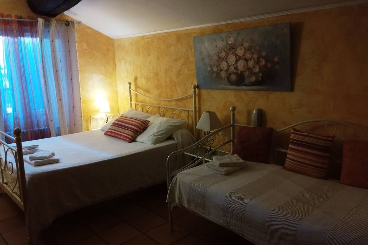 Een slaapkamer met twee bedden, een bloemschilderij aan de wand, en een raam met gordijnen.